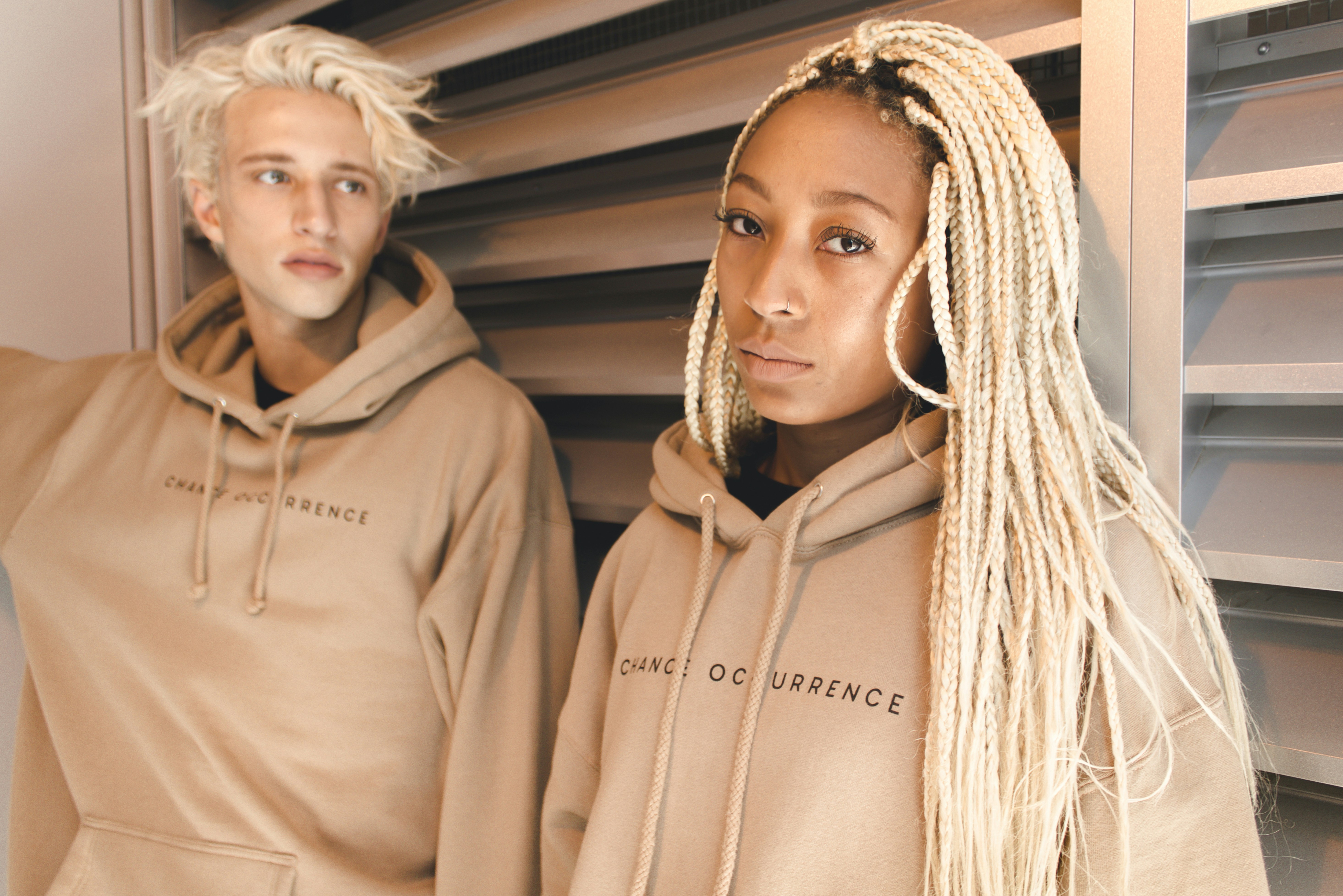 Two models standing side by side wearing beige hoodies